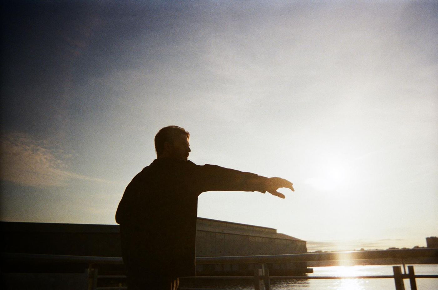Silhouette of a man reaching toward the sun over the water